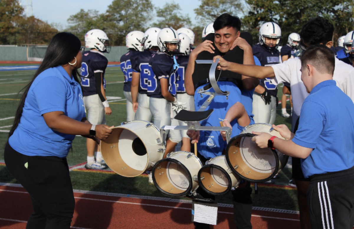 Zatz is supported by his bandmates to help him play the drums upside down during homecoming, balancing both band and his duties as the gladiator.
